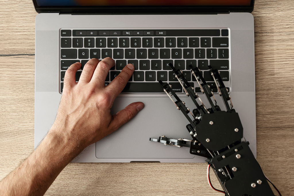 Menselijke hand en robothand op laptop.