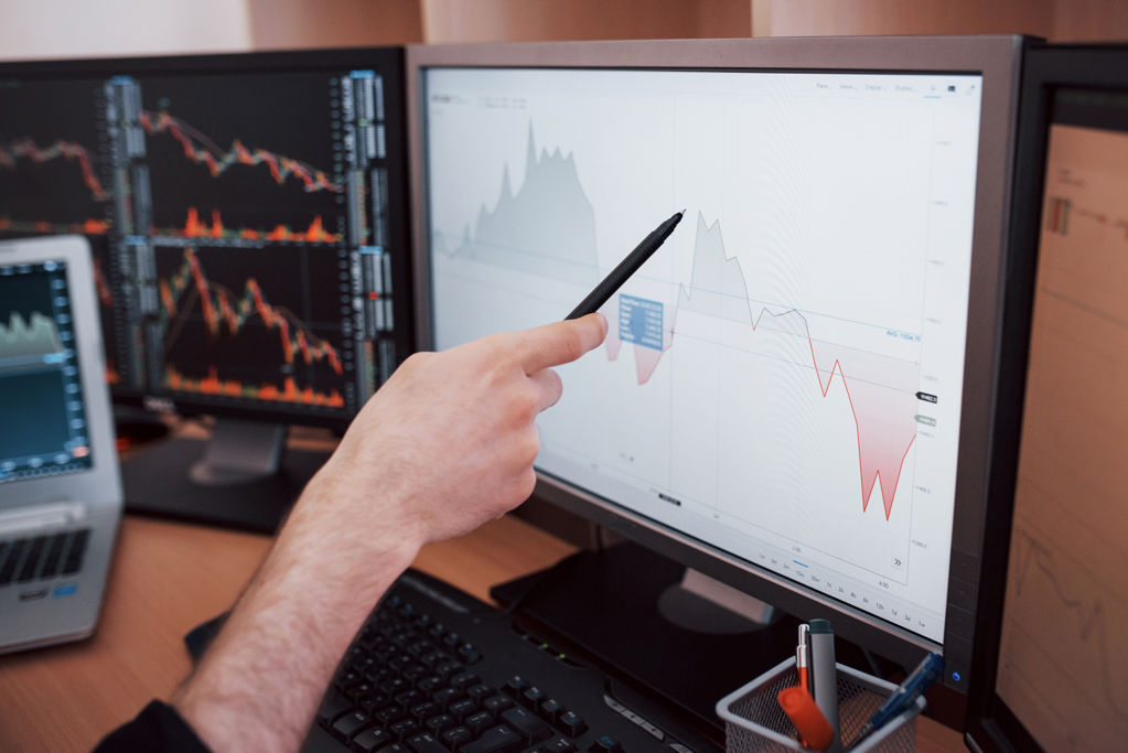 man wijst met pen op grafiek op computer