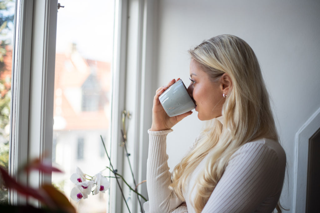 Vrouw die kop thee drinkt en naar buiten kijkt.